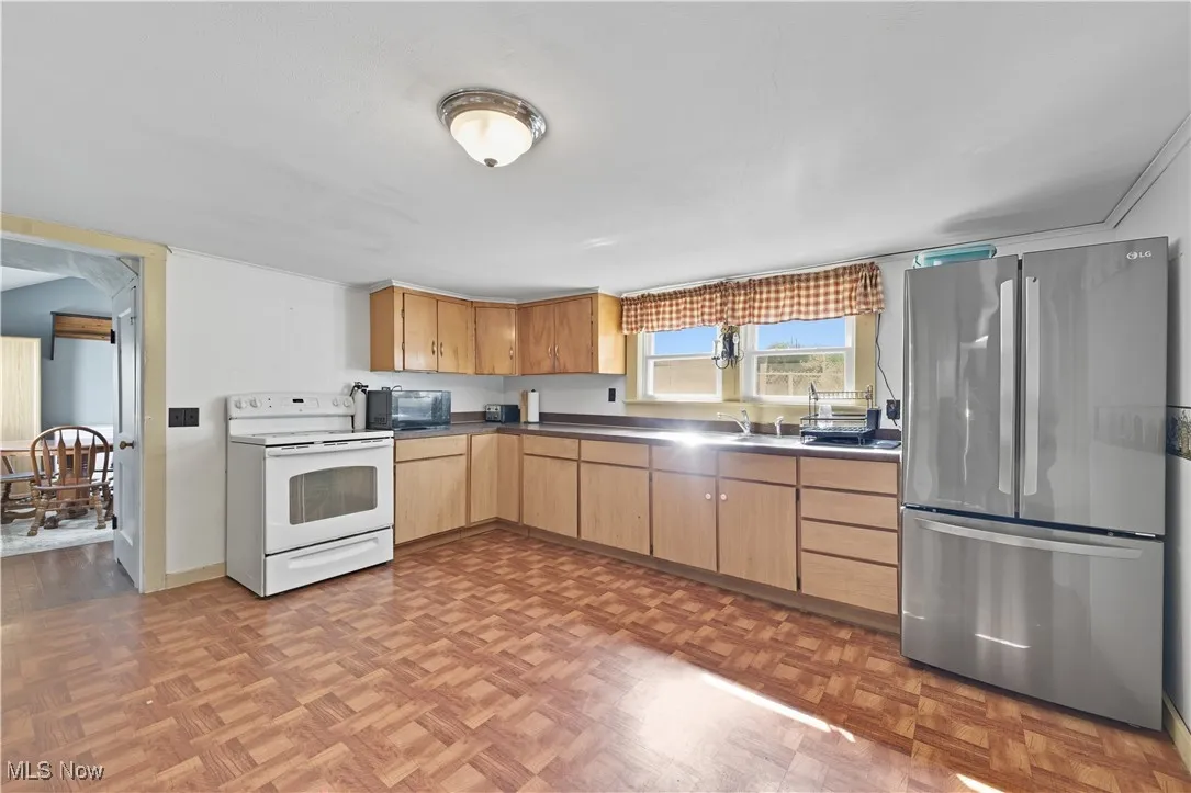 Kitchen featuring freestanding refrigerator, white range with electric stovetop, black microwave, and dark countertops