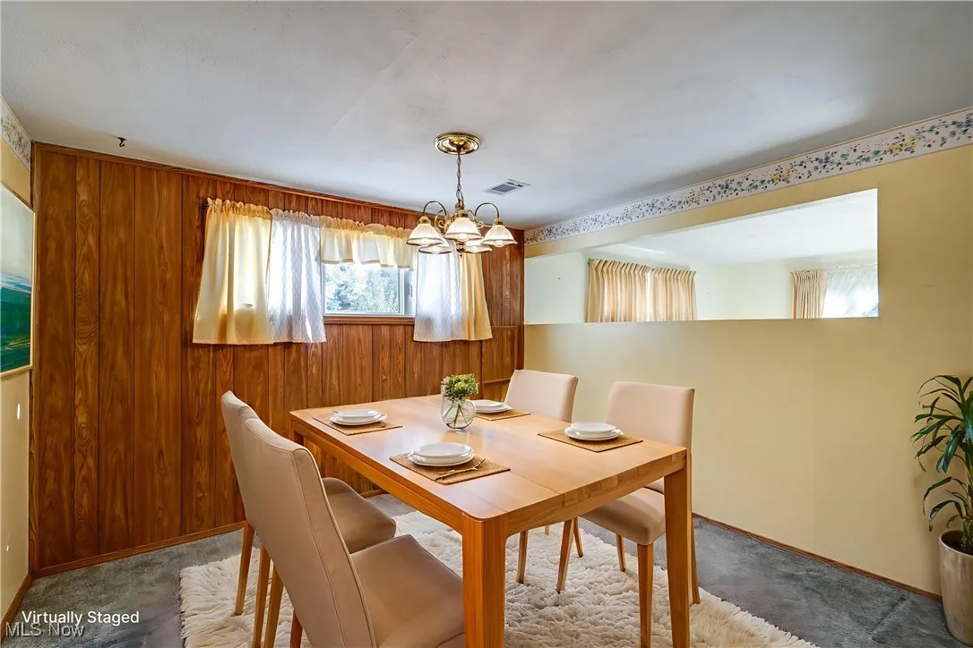 Dining room with a chandelier, wood walls, and carpet flooring
