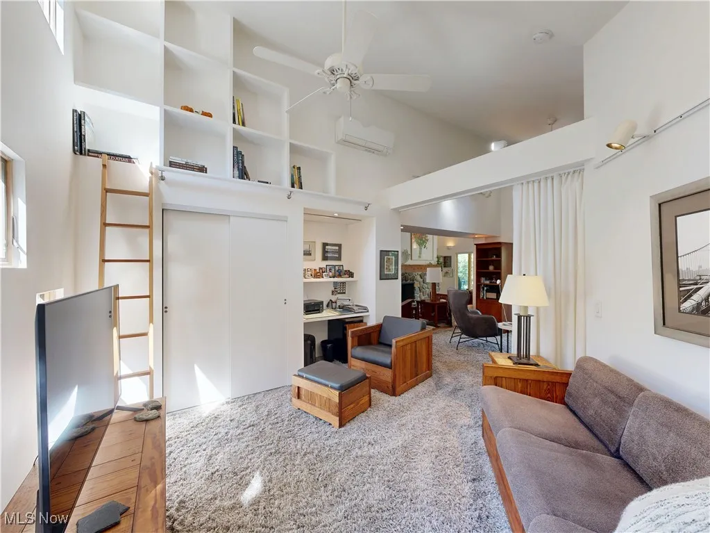 Living area featuring light carpet, ceiling fan, a high ceiling, and a wall mounted AC