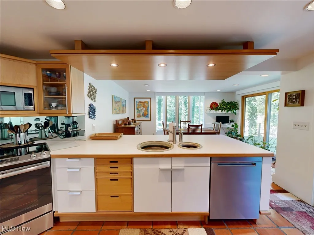 Kitchen featuring recessed lighting, appliances with stainless steel finishes, light countertops, a peninsula, and glass insert cabinets