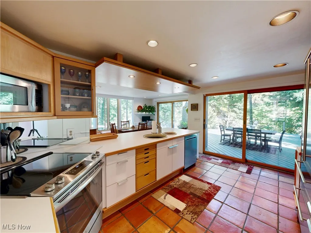 Kitchen with appliances with stainless steel finishes, light countertops, glass insert cabinets, recessed lighting, and light tile patterned flooring