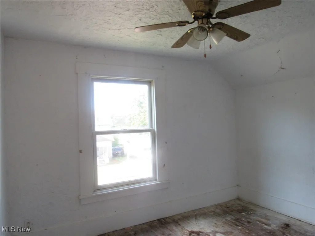 Spare room featuring a textured ceiling, vaulted ceiling, and a ceiling fan