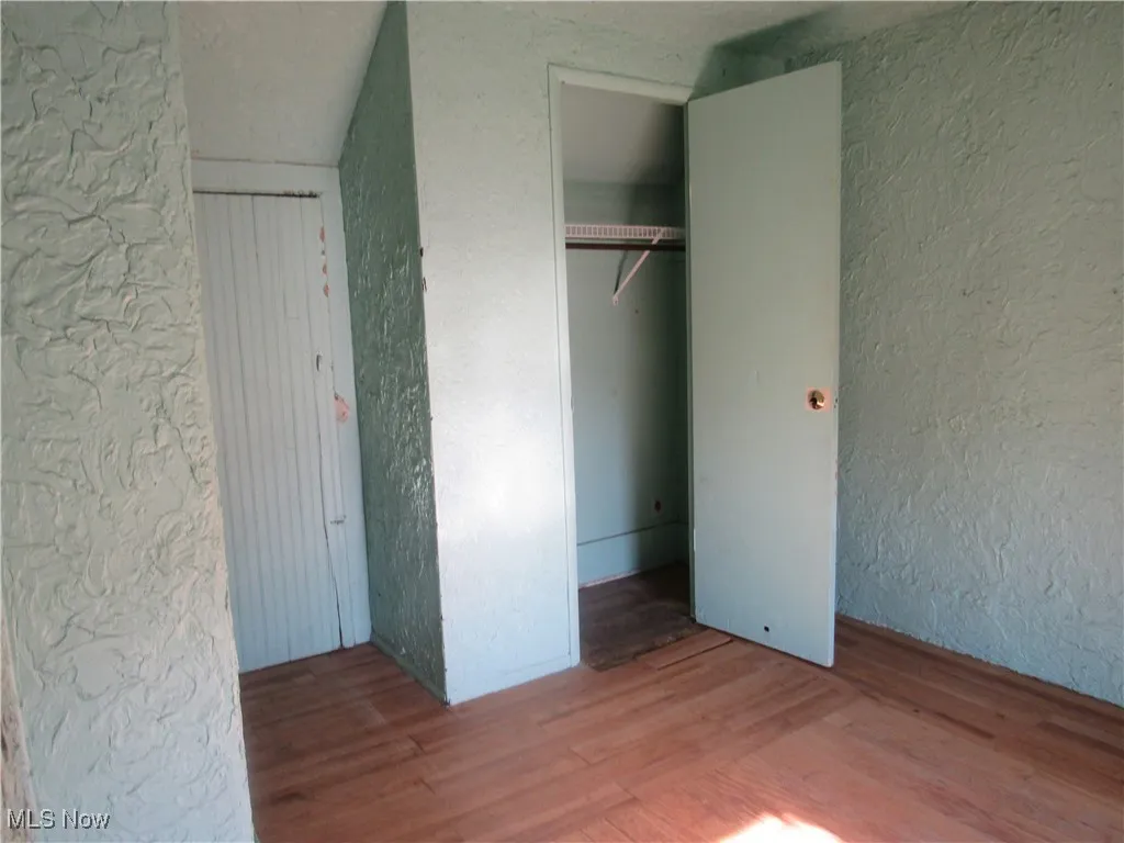 Unfurnished bedroom with a textured wall, wood finished floors, and a closet