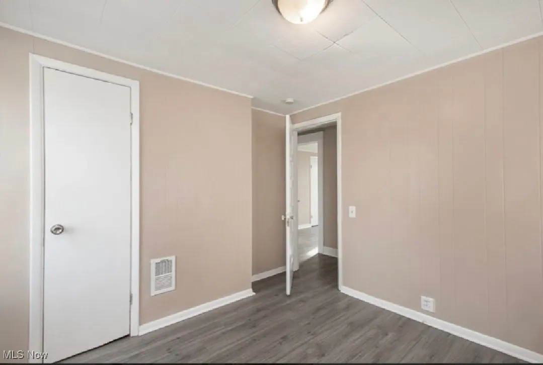 Unfurnished bedroom with dark wood-style flooring and wood walls