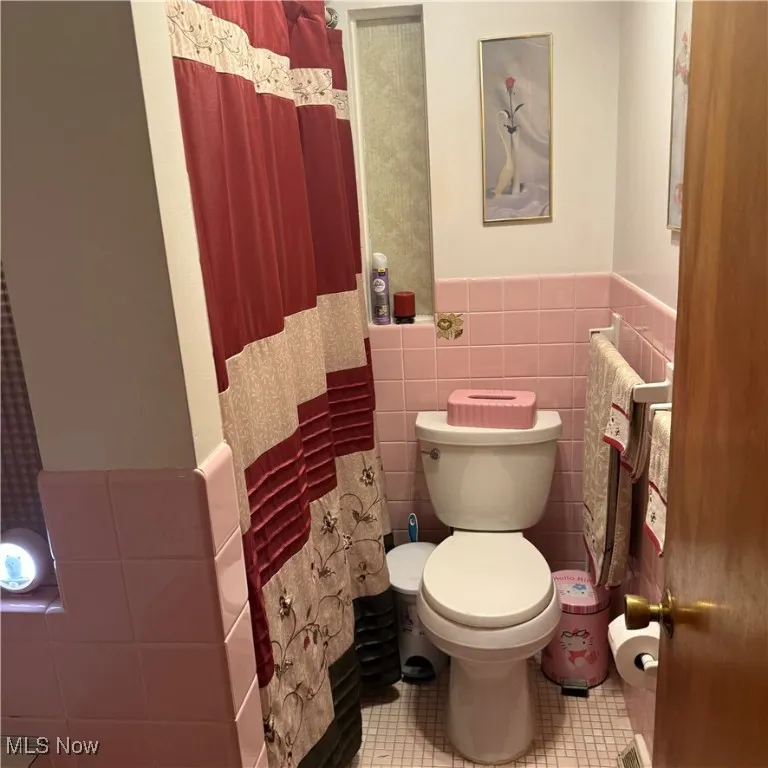 Full bath featuring tile walls, wainscoting, light tile patterned flooring, and a shower with shower curtain