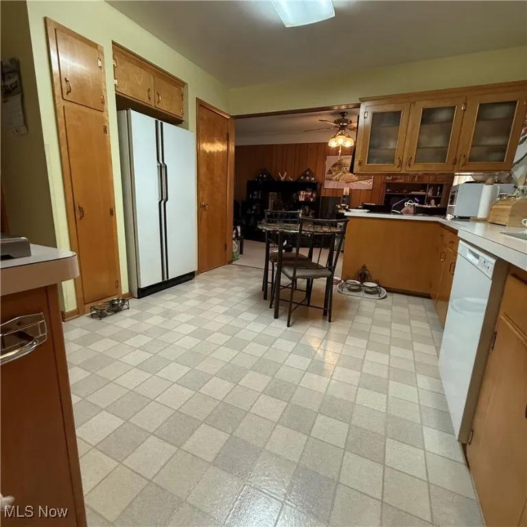 Kitchen with light countertops, white appliances, glass insert cabinets, brown cabinets, and light floors
