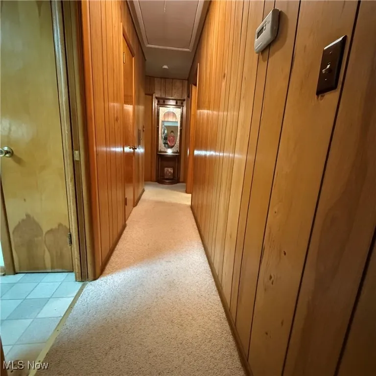 Hallway featuring elevator, wood walls, light colored carpet, and attic access