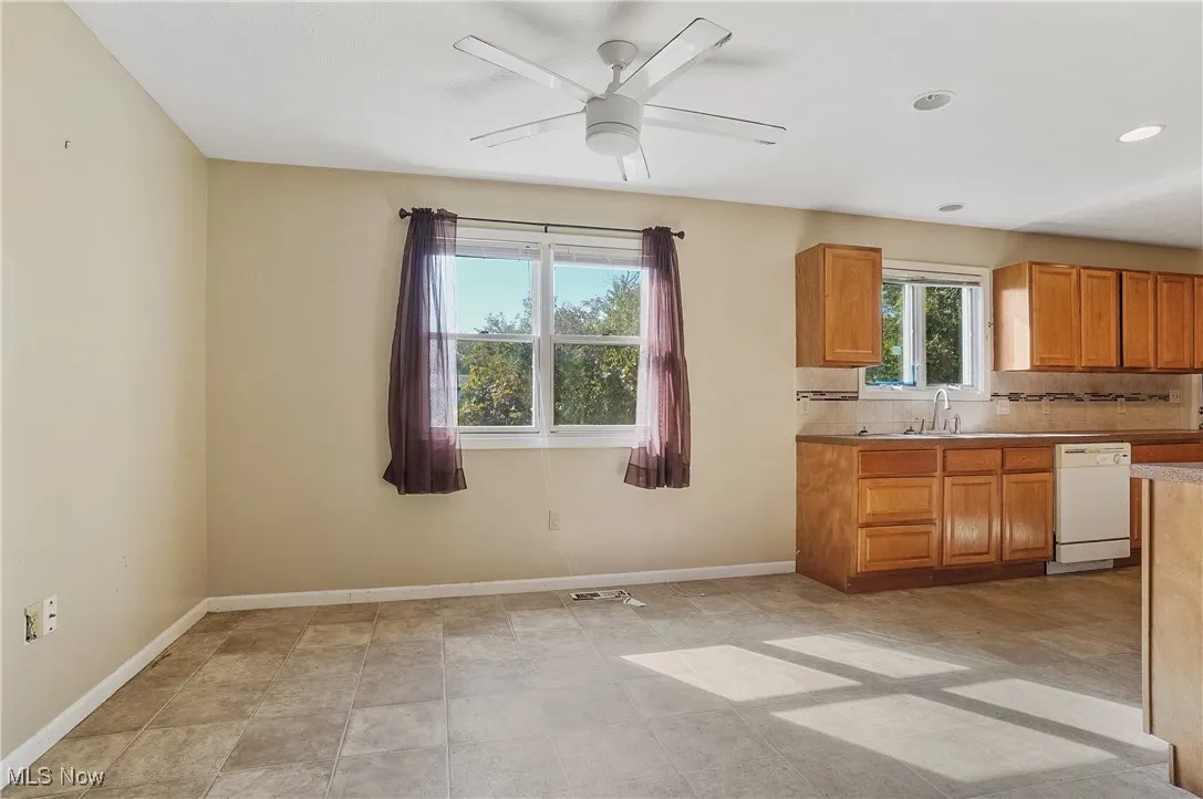 Kitchen featuring brown cabinets, backsplash, white dishwasher, a ceiling fan, and light countertops