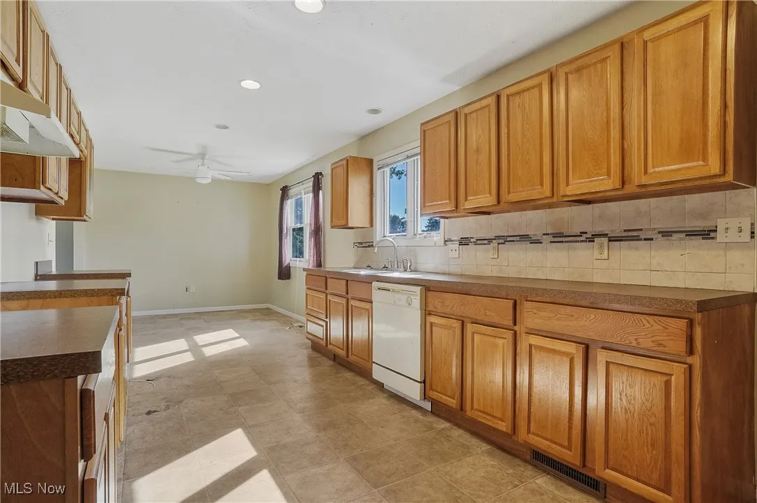 Kitchen with brown cabinetry, tasteful backsplash, dark countertops, white dishwasher, and recessed lighting