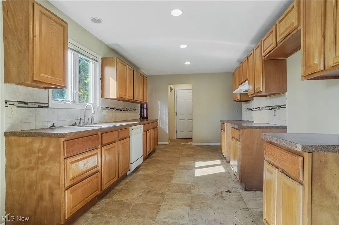Kitchen featuring decorative backsplash, recessed lighting, white dishwasher, dark countertops, and under cabinet range hood