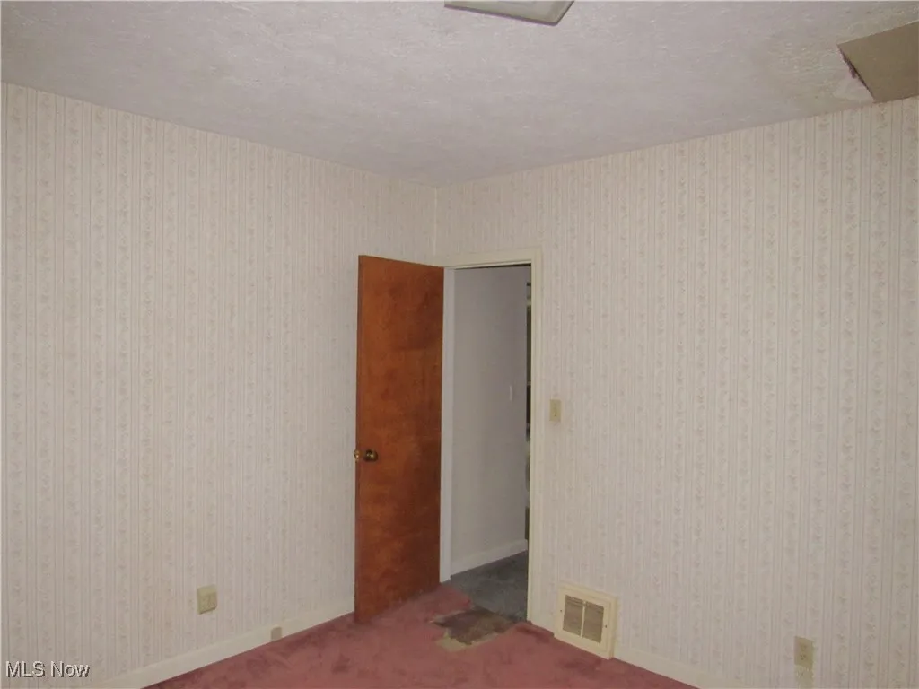 Carpeted empty room with a textured ceiling and baseboards