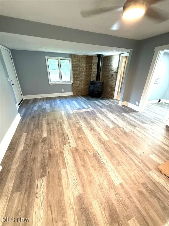 Great room featuring a wood burner, a ceiling fan, light wood-style floors, and brick wall