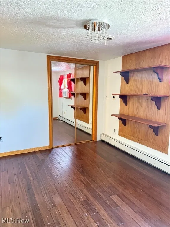 Spare room with a baseboard radiator, a textured ceiling, dark wood-style flooring, and a chandelier