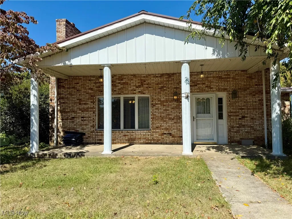 Rear view of property with a lawn, a chimney, and brick siding