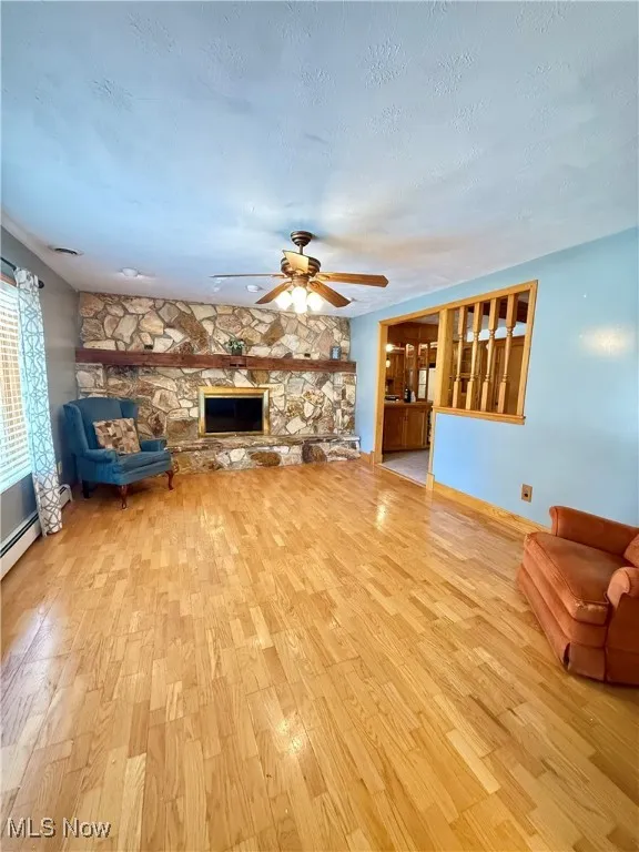 Unfurnished living room featuring a fireplace, light wood-style floors, a textured ceiling, ceiling fan, and a baseboard heating unit