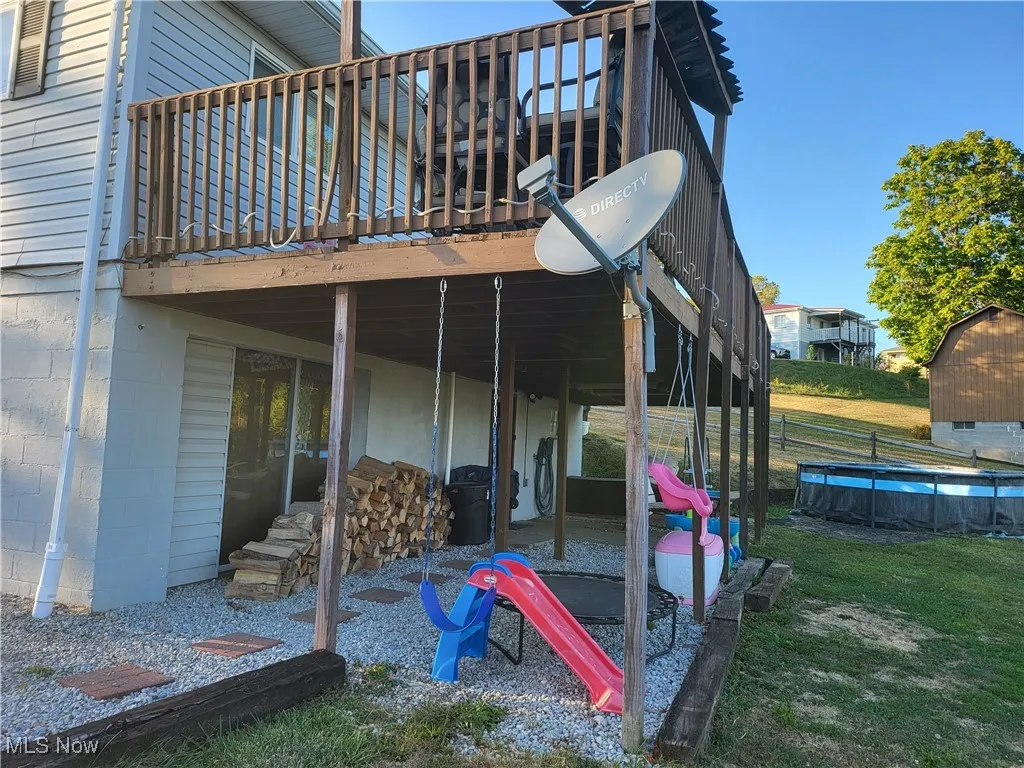 Rear view of property featuring concrete block siding, a patio, a deck, a yard, and a pool
