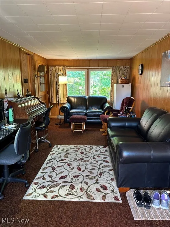 Living area with wooden walls, dark carpet, and a desk