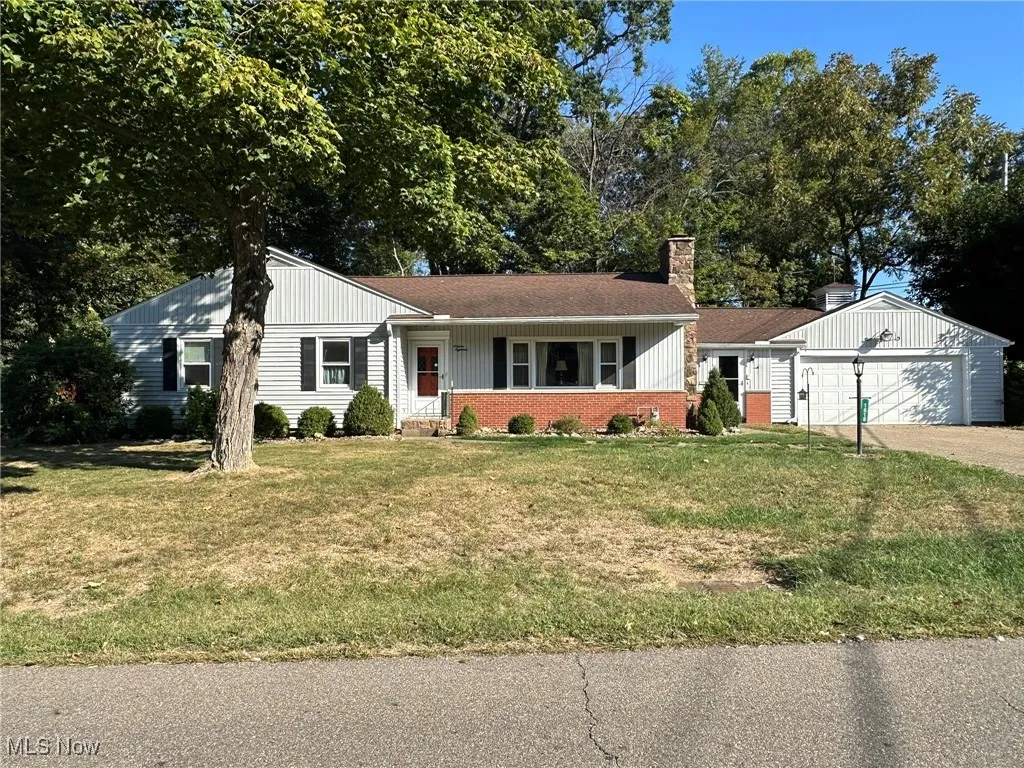 Ranch-style house with a porch, a garage, brick siding, a front lawn, and a chimney