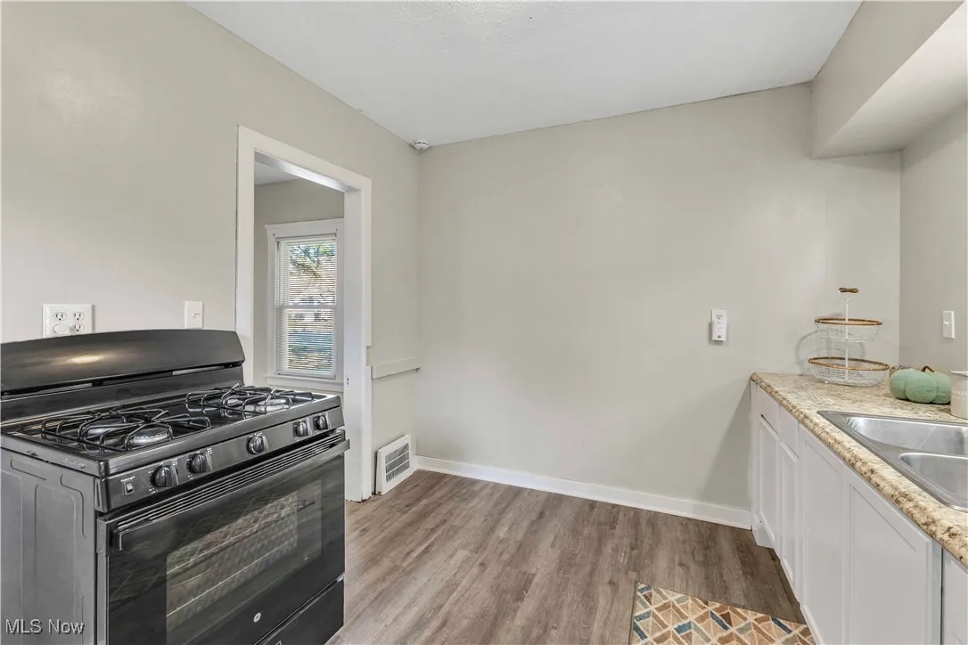 Kitchen with black gas range, white cabinetry, light wood-style flooring, and light stone countertops