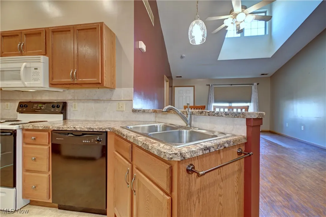 Kitchen featuring white appliances, backsplash, ceiling fan, a skylight, and pendant lighting