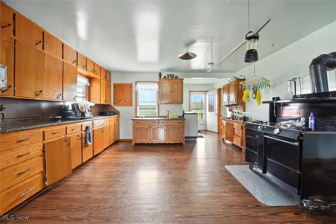 Kitchen with dark wood-style floors, brown cabinetry, dark countertops, and hanging light fixtures