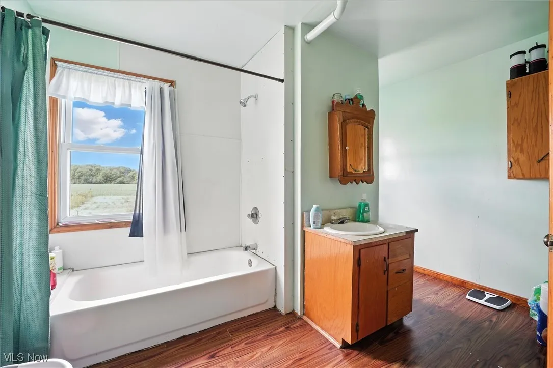 Bathroom featuring shower / bath combination with curtain, dark wood-style flooring, and vanity