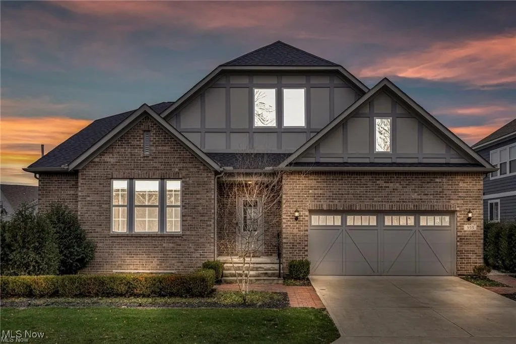 Tudor-style house featuring brick siding, driveway, a garage, a front lawn, and a shingled roof