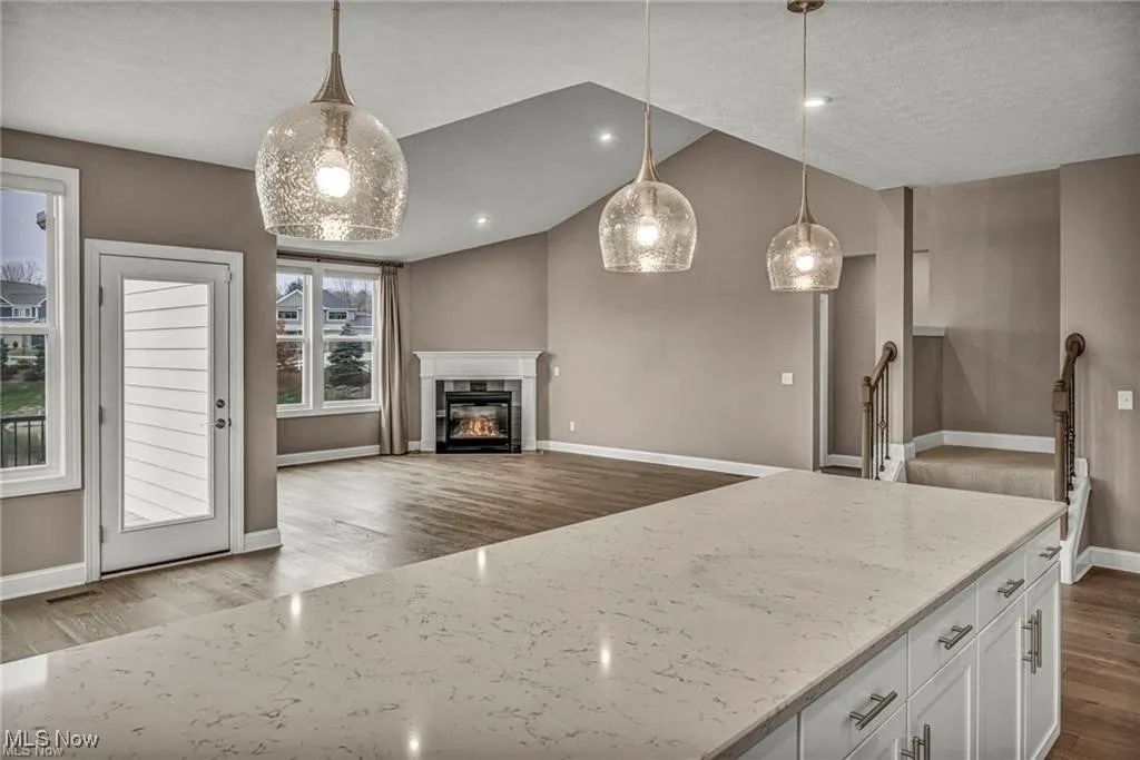 Kitchen featuring vaulted ceiling, hanging light fixtures, light stone countertops, dark wood-style floors, and open floor plan