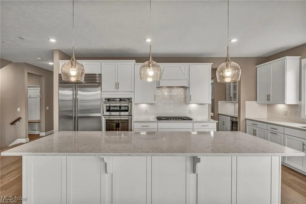 Kitchen with light wood finished floors, stainless steel appliances, white cabinets, a spacious island, and recessed lighting