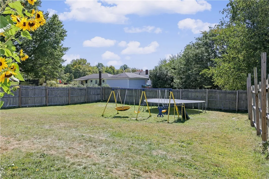 Fenced backyard featuring a playground and a trampoline