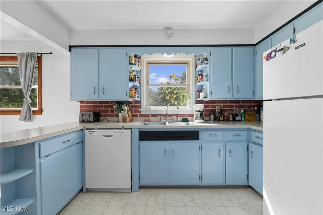 Kitchen with open shelves, white appliances, blue cabinetry, and a peninsula