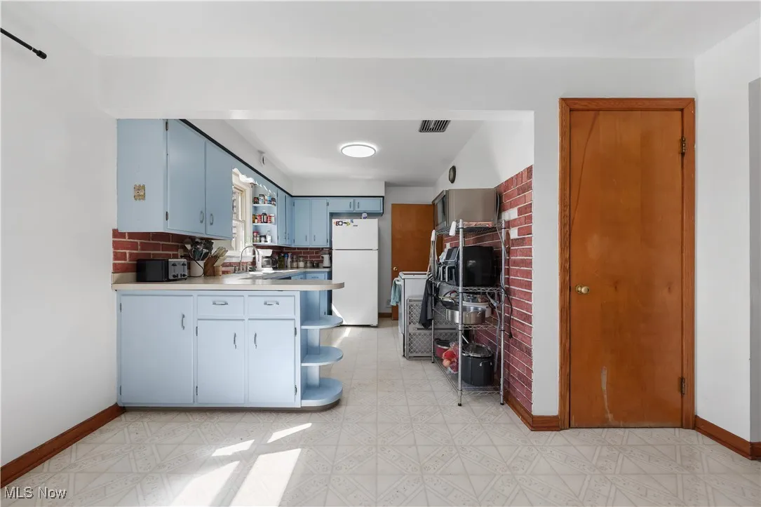 Kitchen featuring open shelves, blue cabinetry, light flooring, light countertops, and white appliances