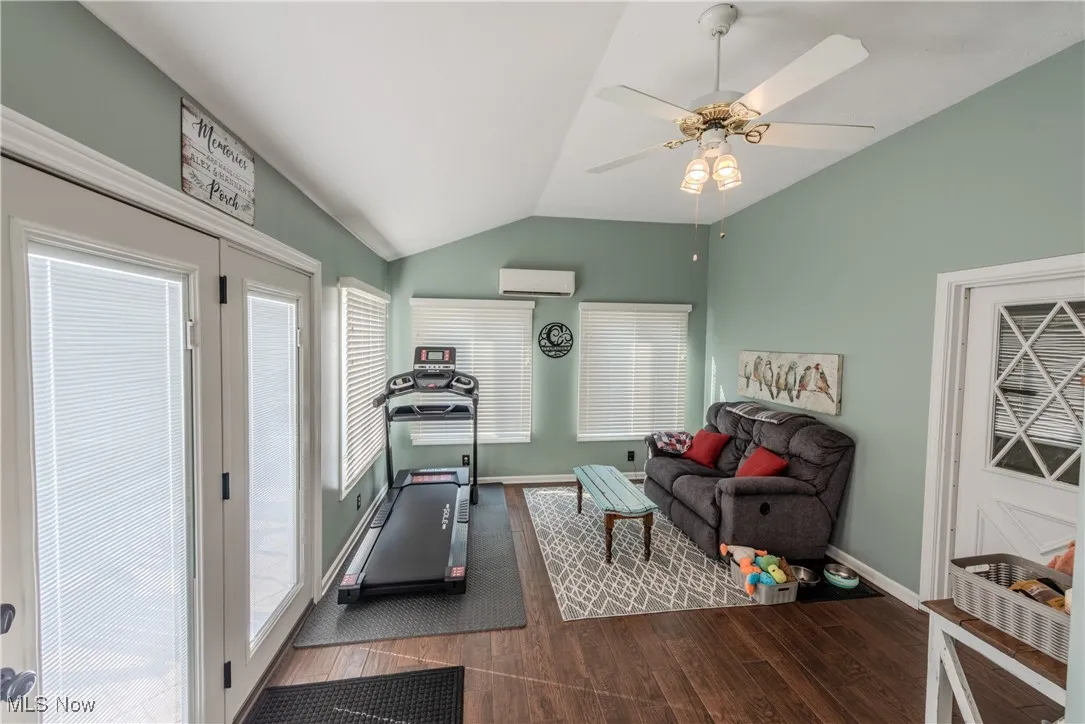 Exercise room with vaulted ceiling, dark wood-style floors, and a ceiling fan