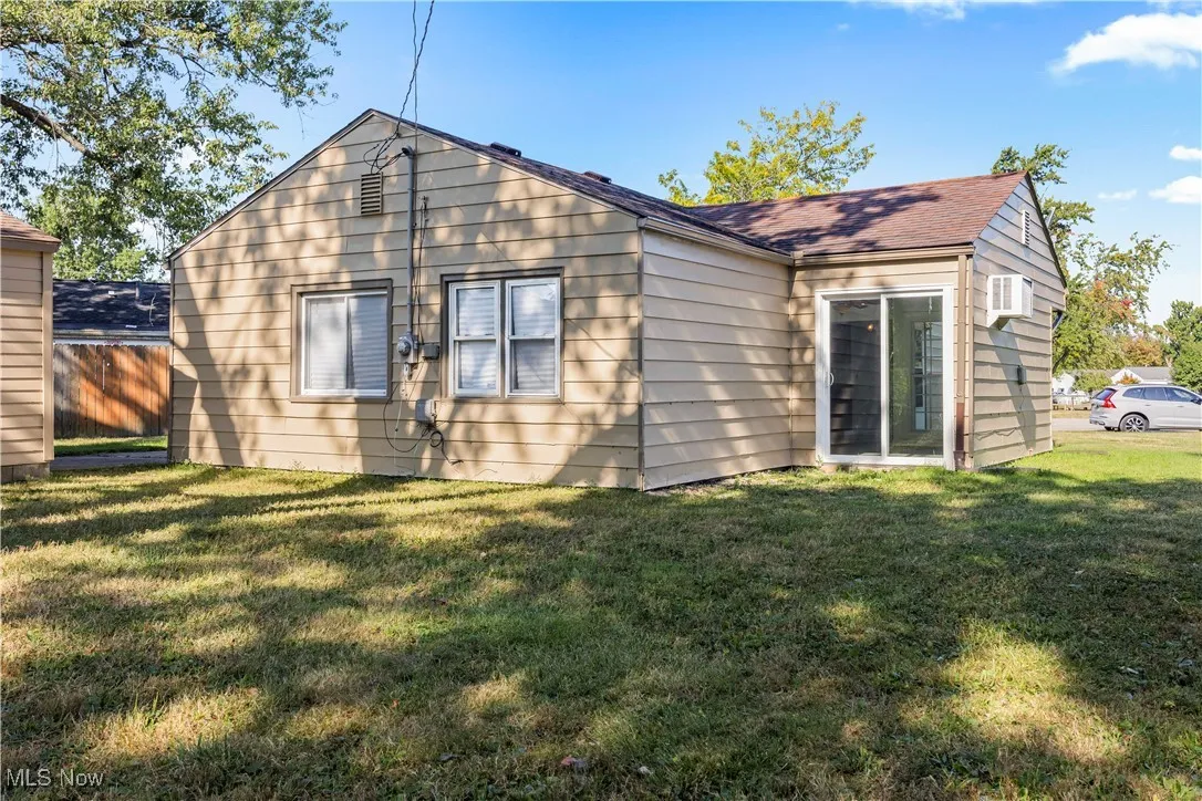 Rear view of property with a lawn and a wall unit AC