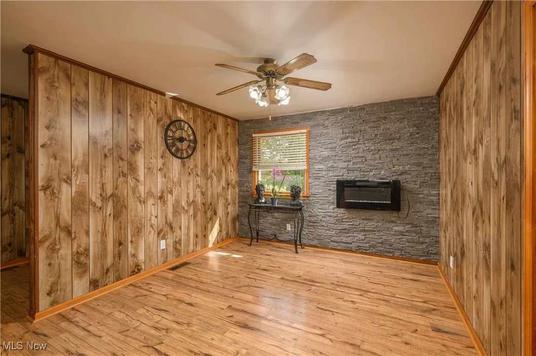 Living area featuring wooden walls, a fireplace, hardwood / wood-style floors, and ceiling fan