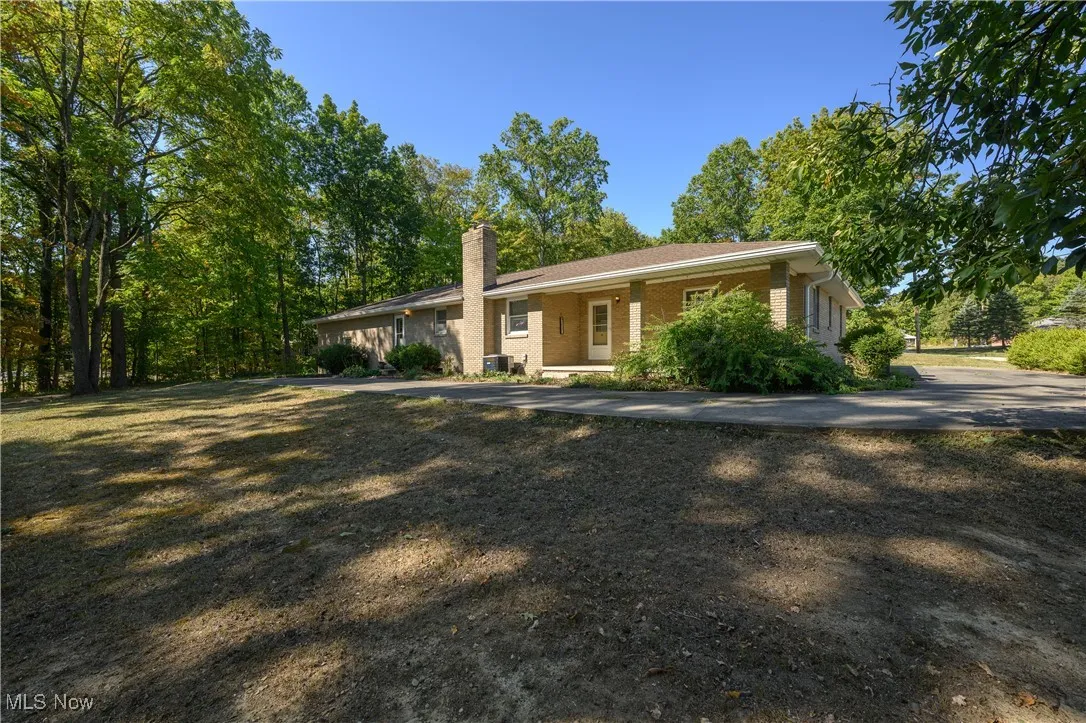 View of front of home featuring brick siding, a chimney, and covered porch