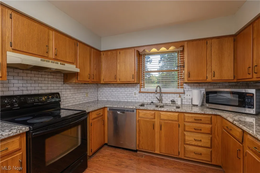 Kitchen featuring stainless steel appliances, backsplash, brown cabinetry, light stone countertops, and light wood finished floors