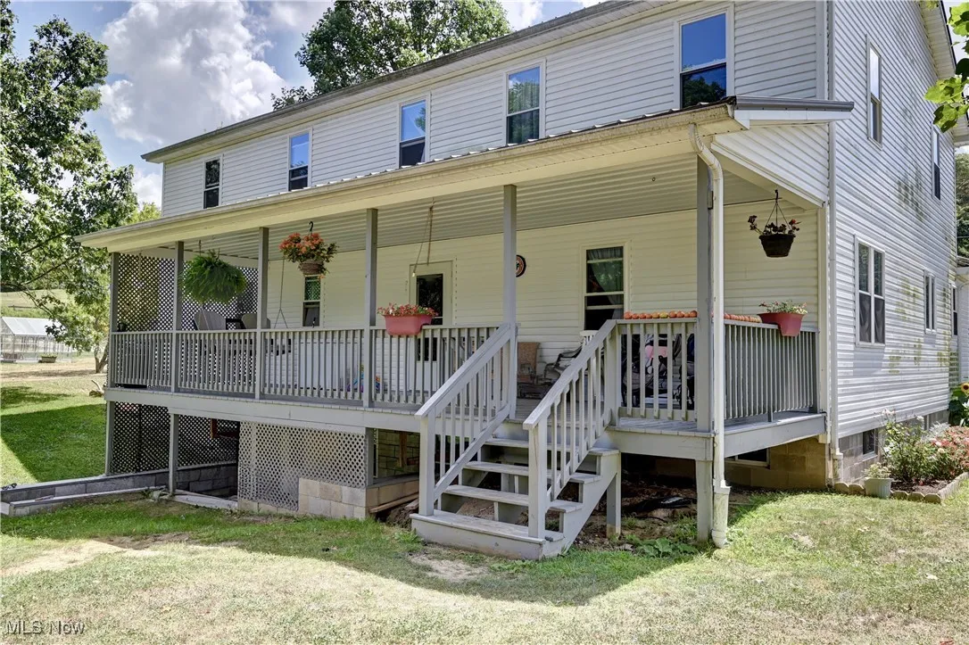 View of back of home with covered porch, a back yard, and stairs