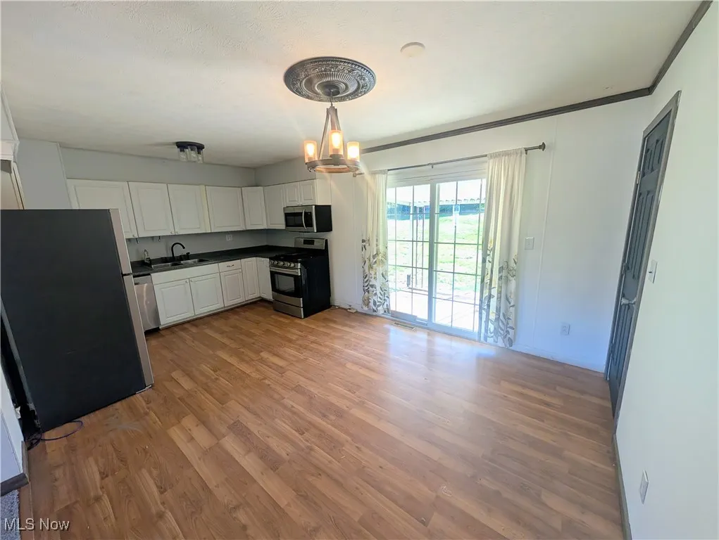 Kitchen with stainless steel appliances, dark countertops, light wood finished floors, white cabinetry, and a chandelier