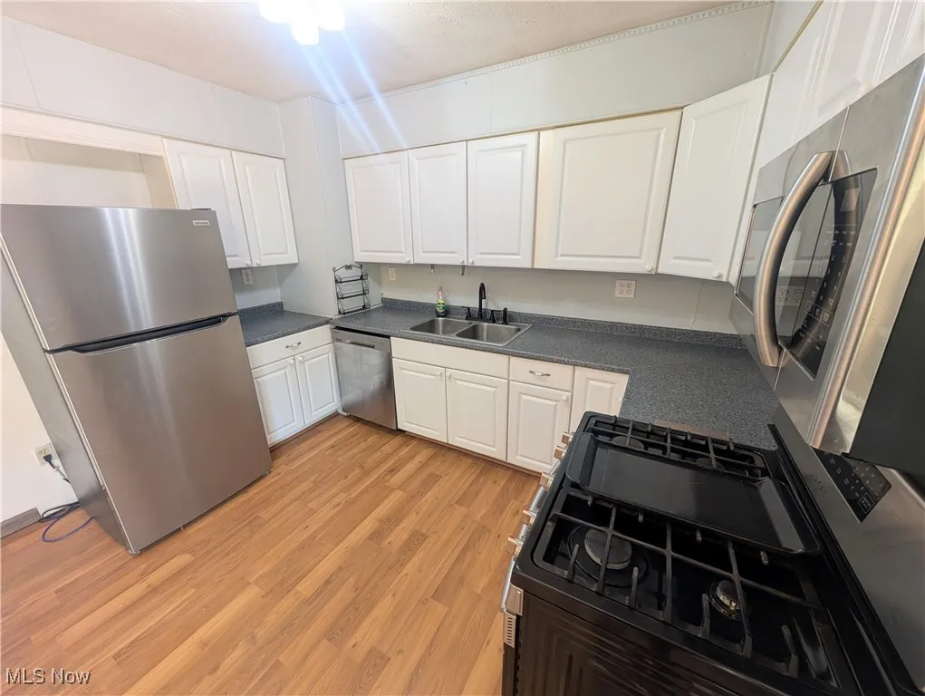 Kitchen with appliances with stainless steel finishes, white cabinetry, dark countertops, and light wood-style floors