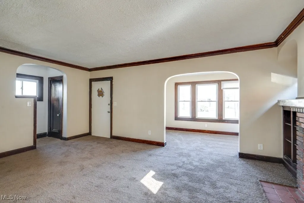 Unfurnished living room with arched walkways, crown molding, healthy amount of natural light, light colored carpet, and a textured ceiling