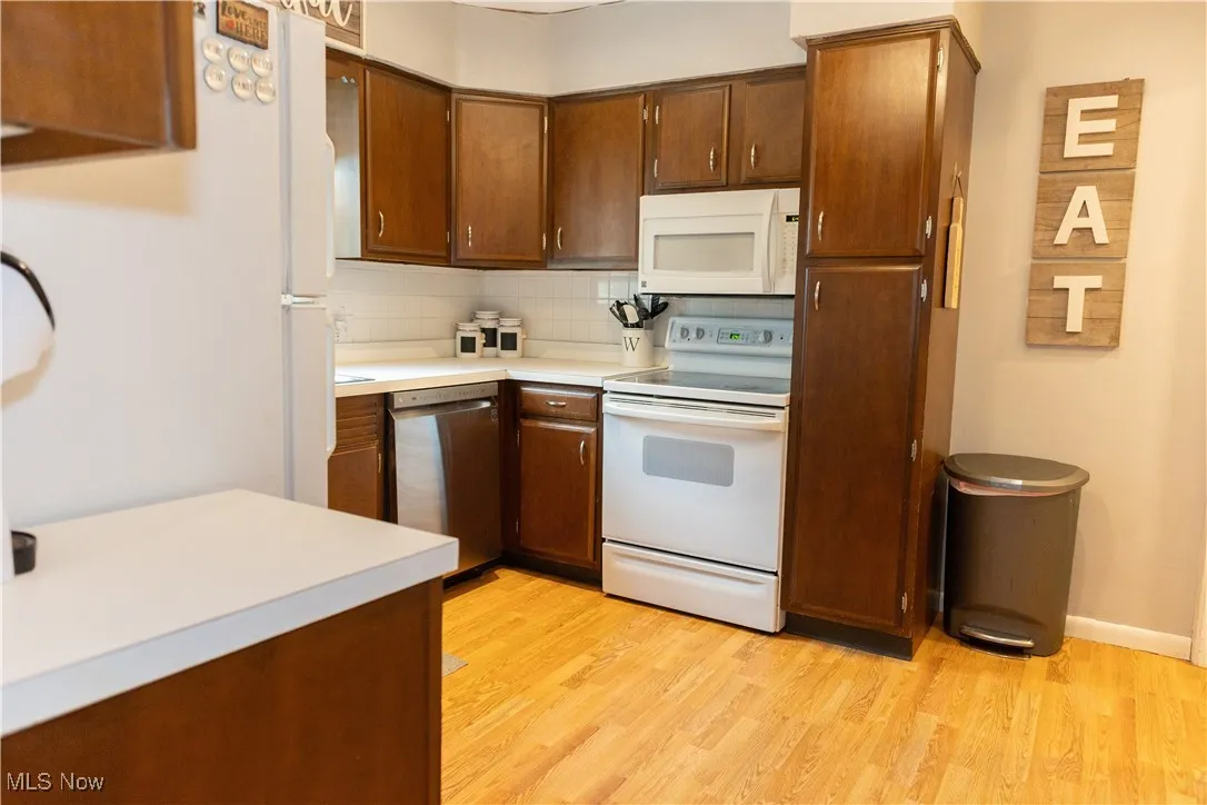 Kitchen featuring white appliances, light countertops, backsplash, light wood-style flooring, and brown cabinetry