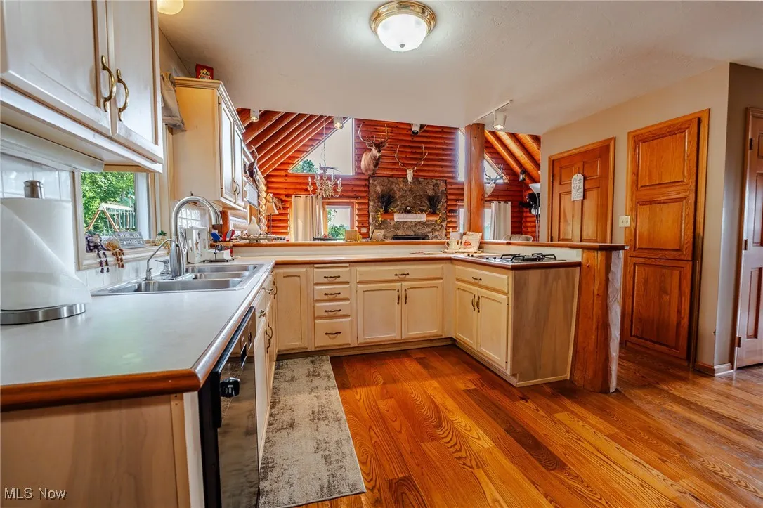 Kitchen with a peninsula, light wood finished floors, rustic walls, light countertops, and black dishwasher