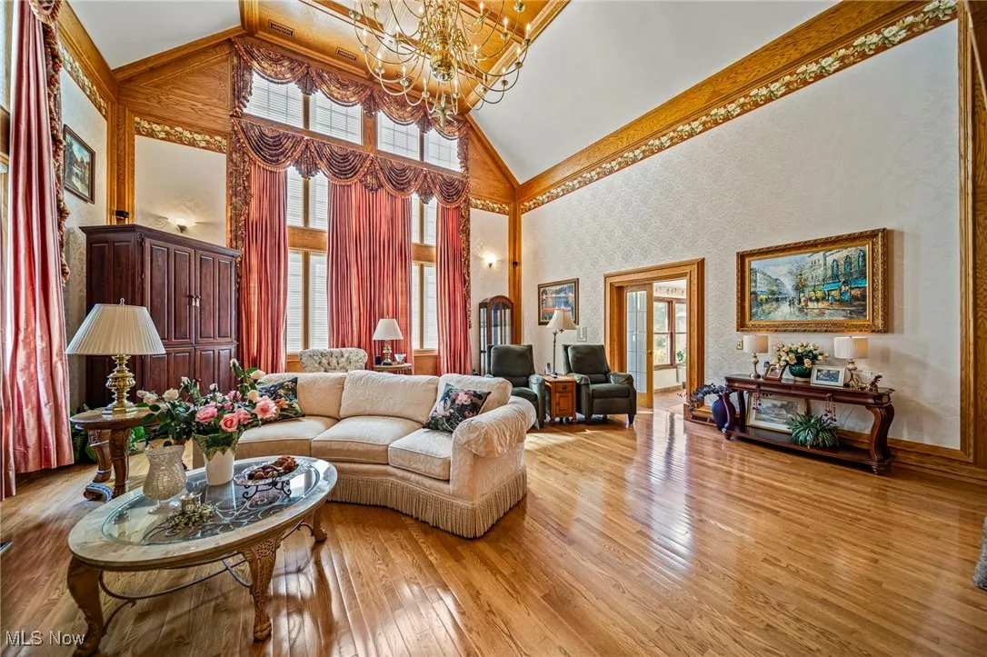 Living area featuring wallpapered walls, high vaulted ceiling, light wood-type flooring, and a chandelier