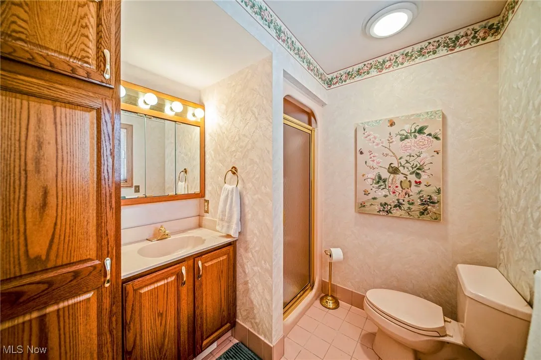 Bathroom featuring light tile patterned floors, vanity, a stall shower, and wallpapered walls