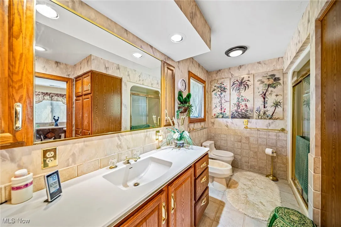 Full bath with tile walls, vanity, light tile patterned flooring, a shower stall, and a bidet