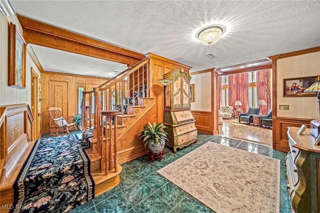 Stairs featuring a textured ceiling, crown molding, tile patterned flooring, wainscoting, and a decorative wall