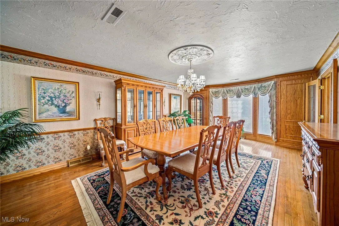 Dining area with ornamental molding, light wood-style floors, wallpapered walls, a textured ceiling, and a chandelier