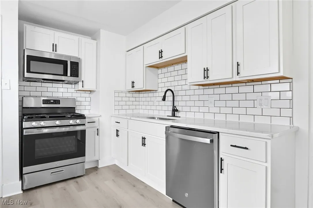 Kitchen with stainless steel appliances, decorative backsplash, light wood-style flooring, and white cabinets
