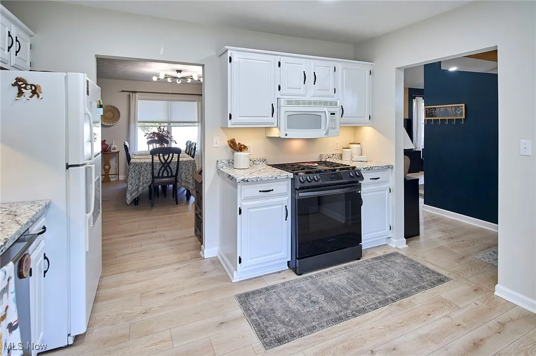 Kitchen featuring white cabinets, white appliances, light wood-style flooring, and a chandelier
